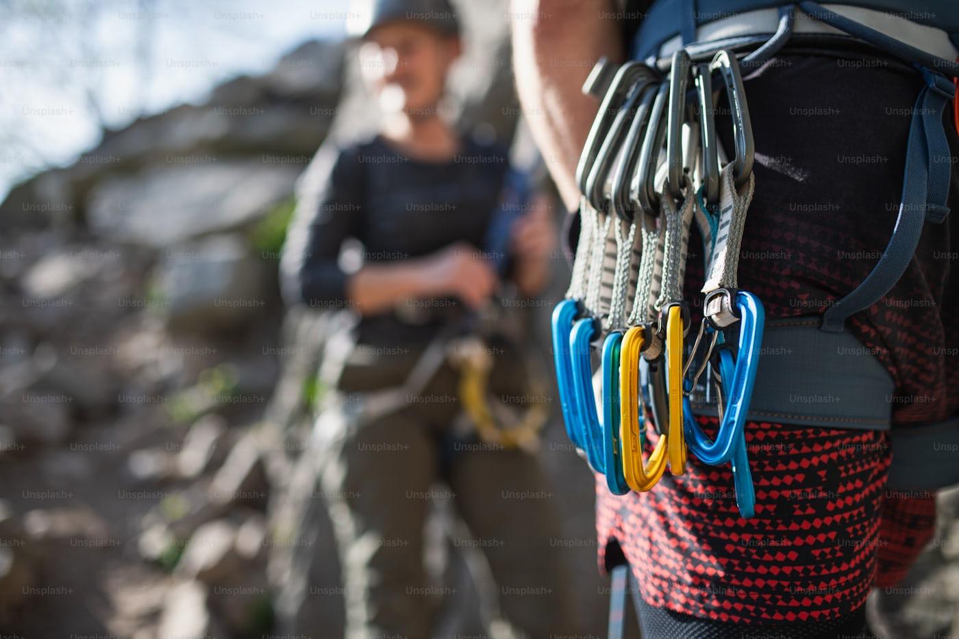 Two climbers preparing at the base of a rock face, harness and carabiners in focus
